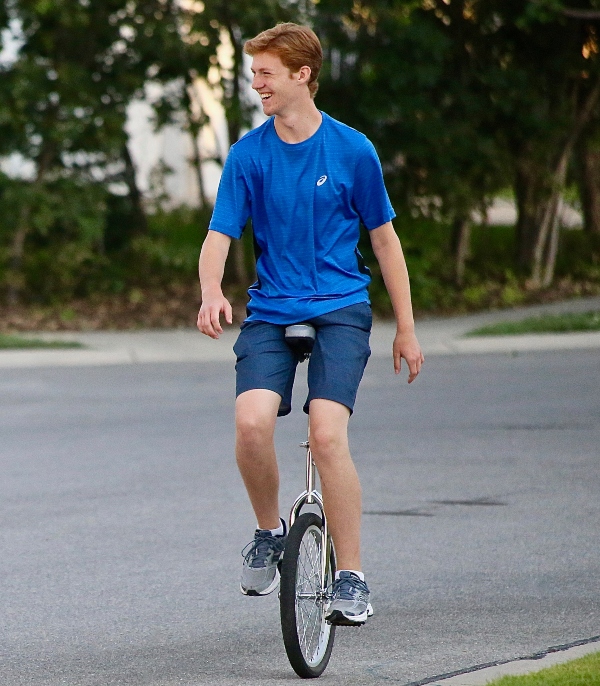 Matthew Bingham riding a unicyle down the street by his home